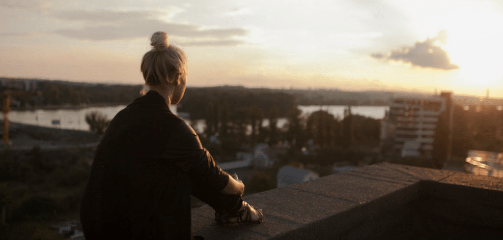 Nainen katsomassa auringolaskua talon katolla.